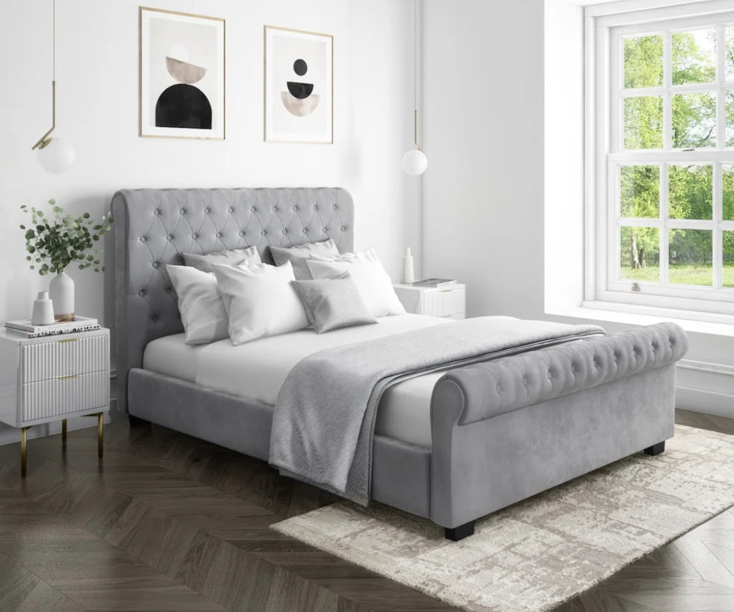 Gray upholstered bed in a bedroom with abstract art on the wall and a window.