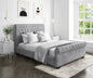 Gray upholstered bed in a bedroom with abstract art on the wall and a window.
